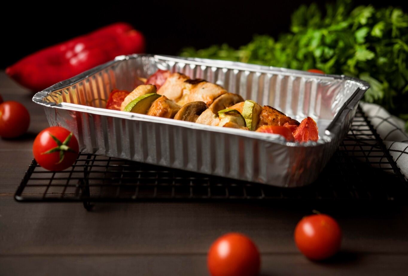 Bandeja de aluminio con brochetas de pollo y verduras recién horneadas