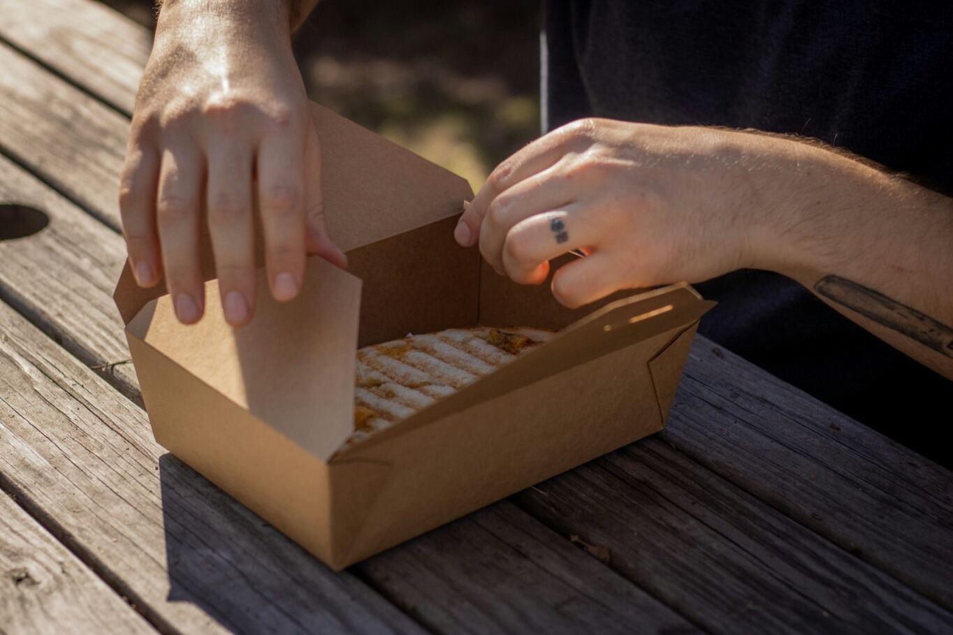 Envase de cartón para llevar abriéndose sobre una mesa de madera